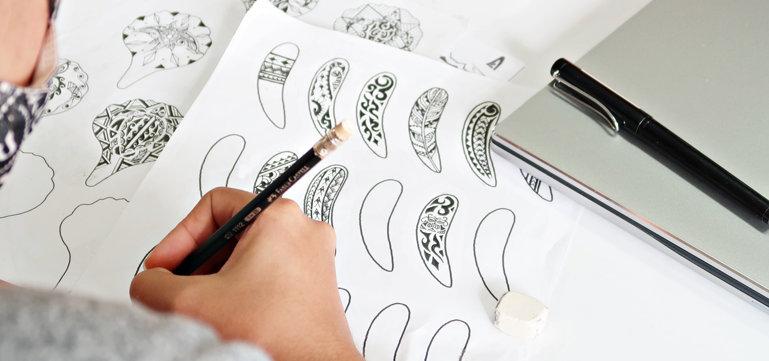 A designer hand-drawing Polynesian-style petal and feather patterns on paper