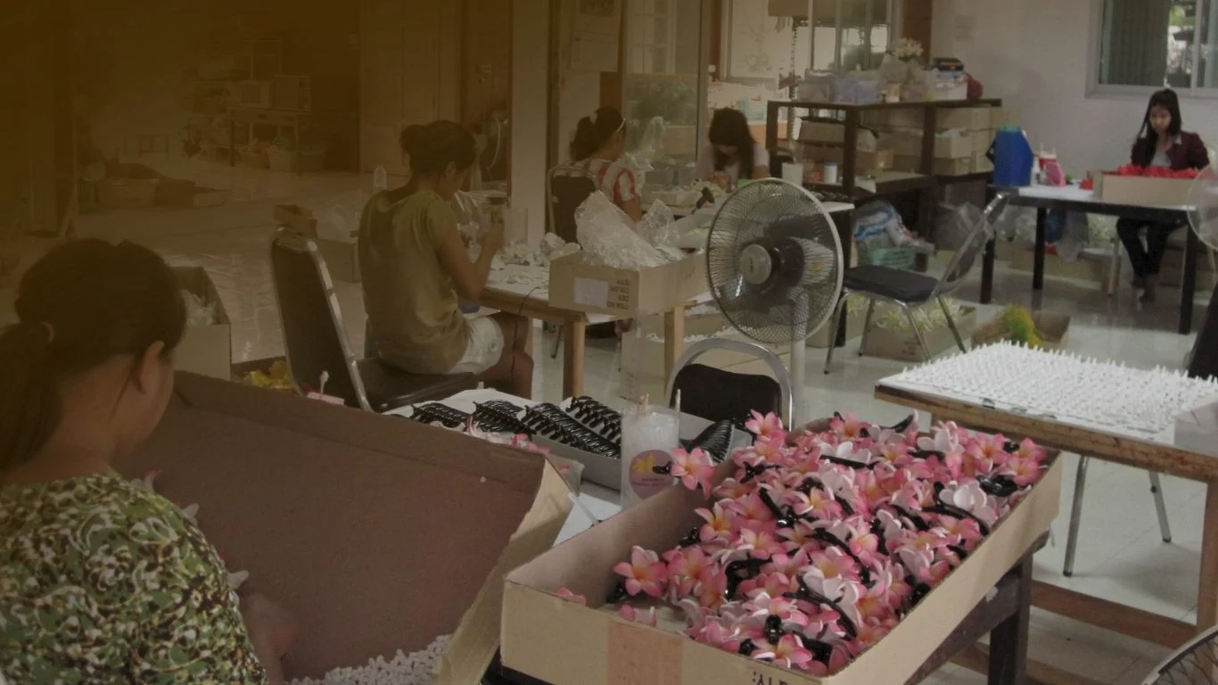 The Foamflora workshop around 2016, artisans assembling pink plumeria hair clips at their tables