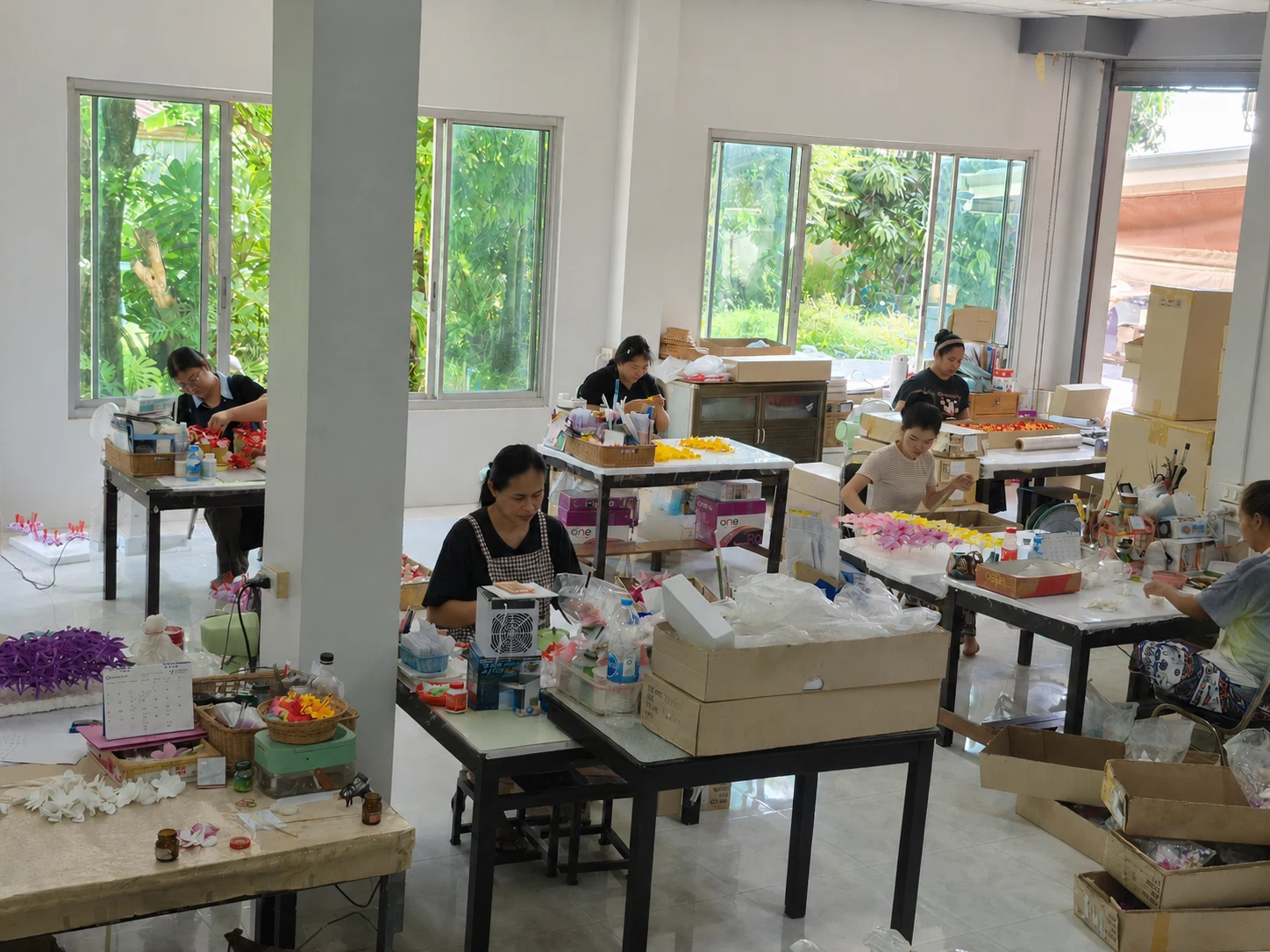 Artisans handcrafting hula flowers at worktables in the sunlit Foamflora workshop