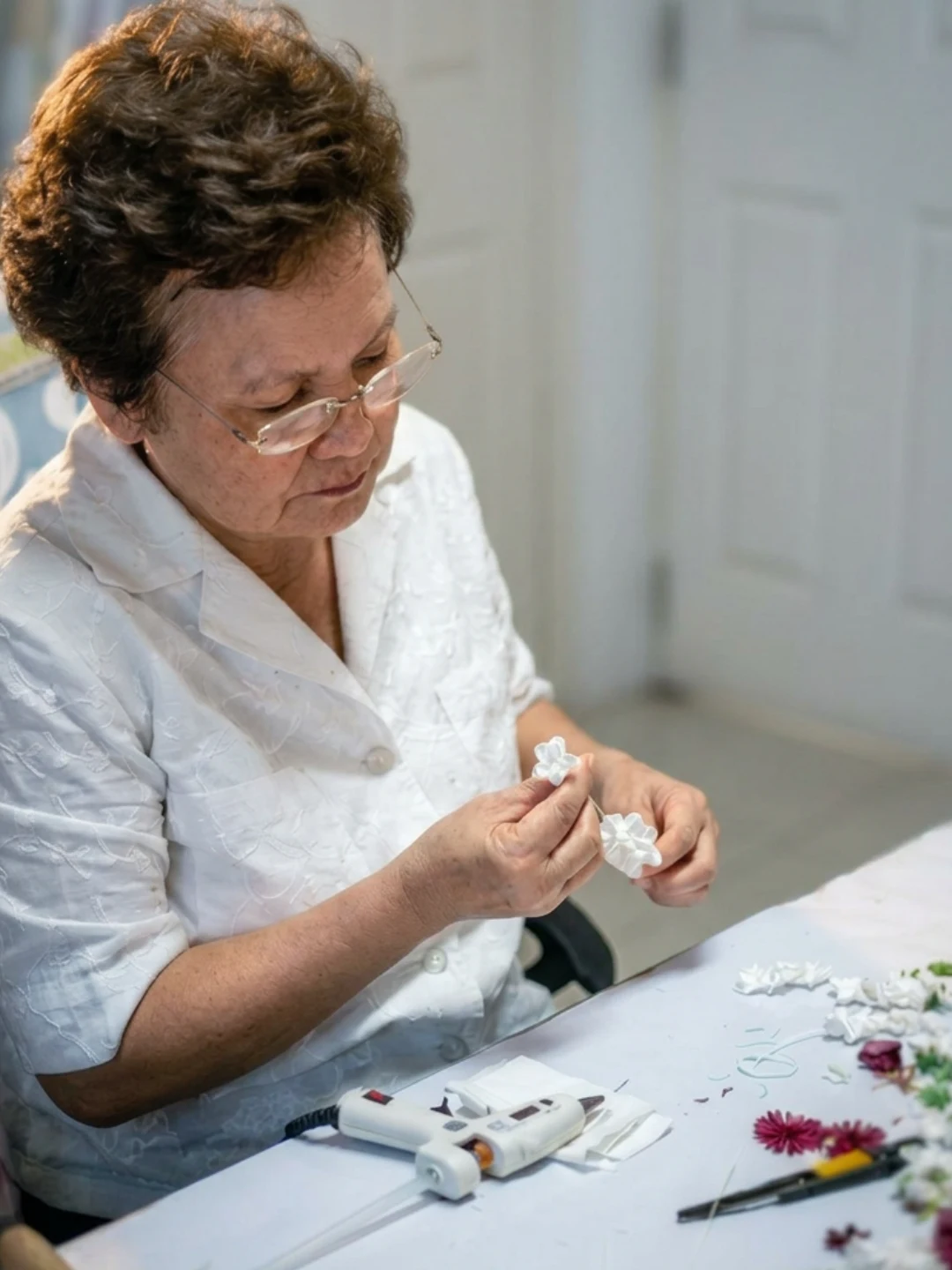 Udomluck, founder of Foamflora, hand-assembling small white flowers at her worktable