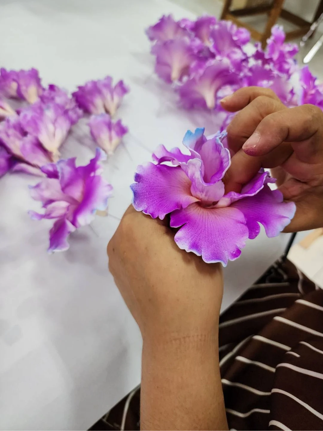 Hands shaping the ruffled petals of a purple hibiscus flower at the Foamflora worktable