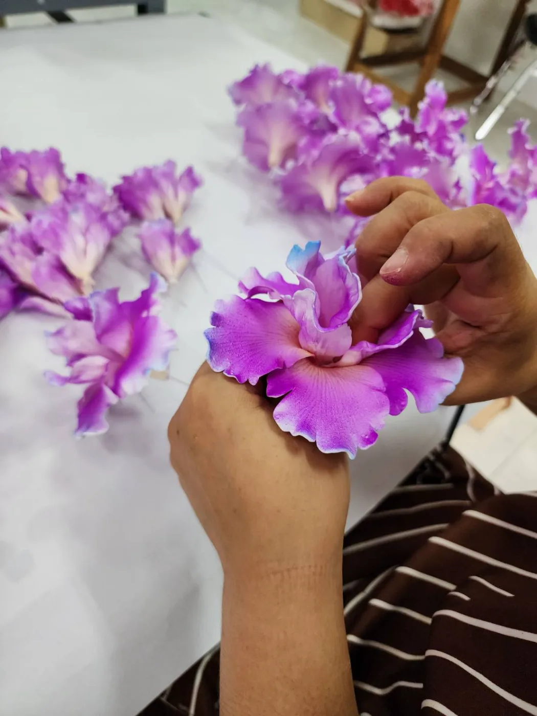 Hands shaping the ruffled petals of a handmade purple orchid