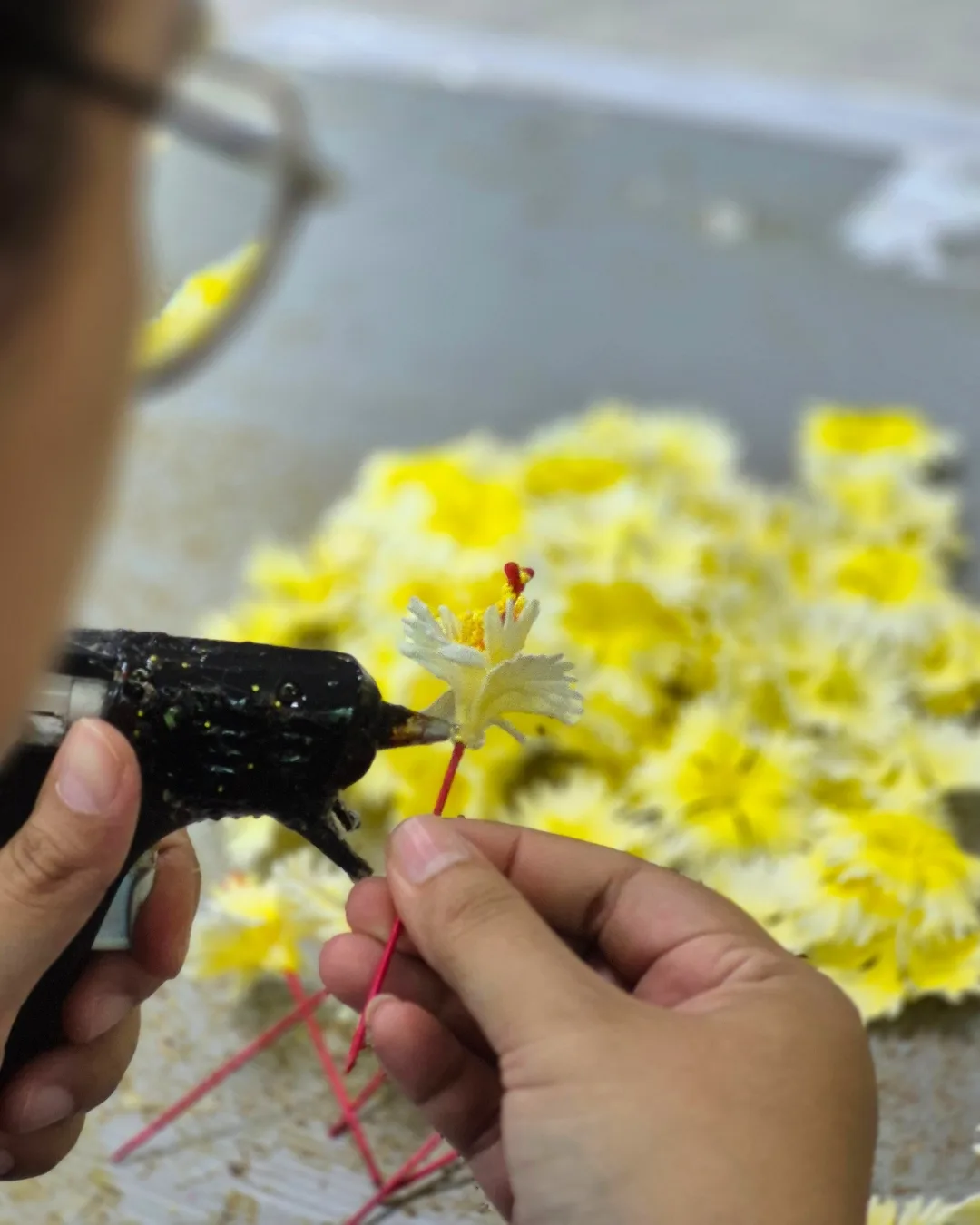 Hands gluing and assembling a handmade yellow hibiscus flower